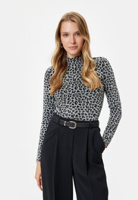 Langärmliges Rollkragenoberteil in Grau mit schwarzem Leopardenmuster, kombiniert mit einer hochgeschnittenen schwarzen Hose und einem schwarzen Gürtel mit einer silbernen Schnalle.
