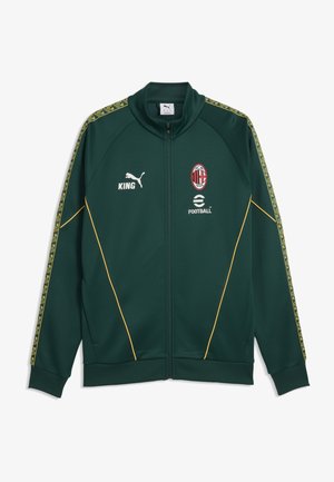 Dunkelgrüne Sportjacke mit hohem Kragen, gelben Akzentlinien und gemusterten Seitenstreifen. Mit weißem Puma-Logo und Team-Emblem auf der Brust.