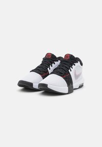 Scarpe sportive in bianco e nero con tessuto in rete e collarino imbottito. Presentano un logo e dettagli rossi, con sovrapposizioni nere testurizzate e suola in gomma.