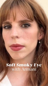 Nærbilde av et ansikt med myk røykfylt øyemakeup, naturlig hud med fregner, og middels langt, rett, rødbrunt hår. Små øredobber er synlige.