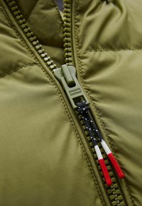 Grön isolerad jacka med dragkedja, med en texturerad yta och kontrasterande dragkedjehandtag i röd och vit.