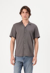 Chemise à manches courtes, gris foncé, boutonnée, en tissu léger, coupe décontractée, avec une texture douce et un col à revers. Associée à un jean bleu clair.