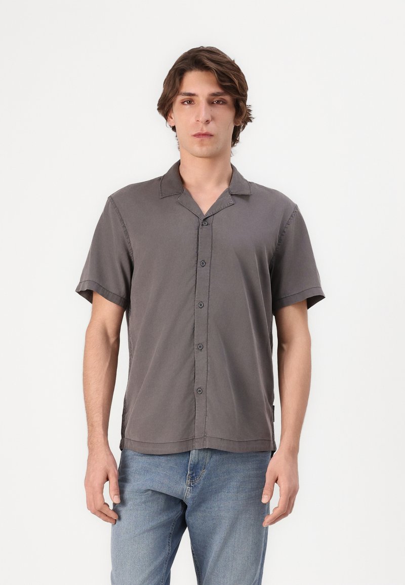 Chemise à manches courtes, gris foncé, boutonnée, en tissu léger, coupe décontractée, avec une texture douce et un col à revers. Associée à un jean bleu clair.