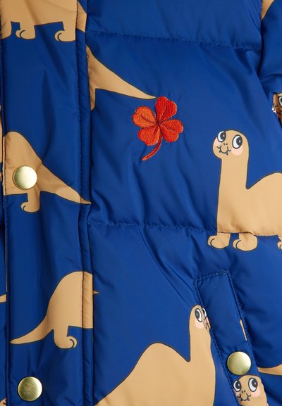 Blue puffer jacket with beige dinosaur prints, featuring gold snap buttons and red embroidered four-leaf clover detail. Soft textured fabric.