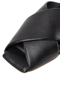 Sandalo in pelle nera con design a strisce incrociate, punta aperta, suola piatta e dettagli testurizzati sulla superficie del materiale.