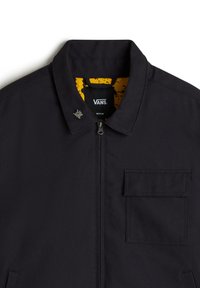 Schwarze Vans-Jacke mit Frontreißverschluss, Klappbrusttasche, kleinem metallischen Pin am Kragen und gelb gemustertem Innenfutter.