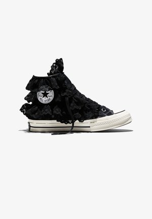 Zwarte hoge Converse-sneaker met witte zool, versierd met gelaagde zwarte kanten ruches rond de enkel en een logopatch.