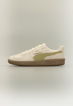 Baskets beiges Puma Palermo avec une bande vert olive, semelle marron, lacets et marquage sur le côté et le talon, présentées en vue de profil sur fond neutre.