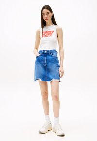 Sleeveless white top with red graphic, paired with a blue denim mini skirt featuring distressed edges and a classic five-pocket design.