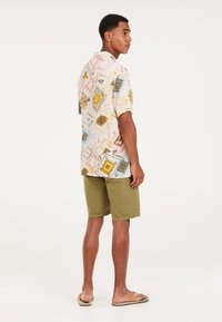 Camisa de manga corta con un estampado geométrico en amarillo, rosa y azul, combinada con pantalones cortos verde oliva y chanclas beige.