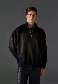 Svart zip-up sweatshirt med hög krage, lös passform, texturerad tyg och framficka. Utrustad med en silverring som dragkedjeaccent.