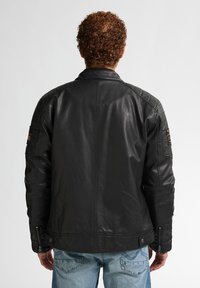 Chaqueta de cuero negro con textura acolchada, acentos en las mangas con cremallera y parches en los hombros. Diseño simple y ajustado.