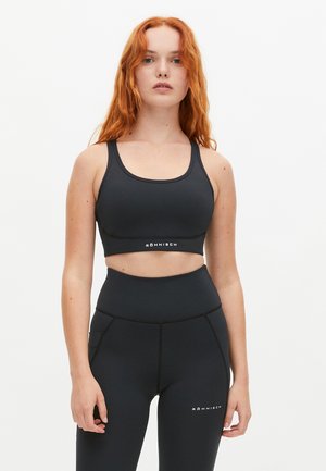 Zwarte sportieve crop top van glad, rekbaar materiaal met een ronde halslijn en uitsnijding. Voorzien van een logo aan de zoom. Hoge taille zwarte leggings.