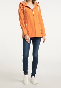 Oranžová bunda s kapucí a kontrastním bílým zipem a tkaničkami, s dvěma předními kapsami a reflexními akcenty. Nositá přes modré džíny.