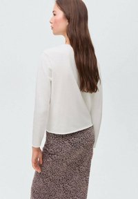 Vit långärmad topp med en kortad bakdesign, i kombination med en mörk blommönstrad kjol som har en mjuk matt textur.