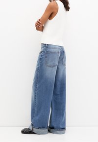 Szerokie niebieskie dżinsy wykonane z denimu, o wyblakłym wykończeniu, z dużymi tylnymi kieszeniami i podwiniętymi mankietami. W połączeniu z dopasowanym białym topem na ramiączkach.