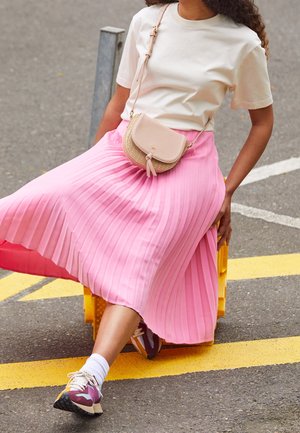 Rosa plisserad kjol, beige topp och stiliga sneakers. Accessoarer inkluderar en liten beige crossbody-väska med en strukturerad design.