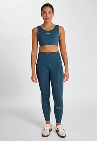 Ein sportlicher BH in Türkis und hochgeschnittene Leggings aus elastischem Stoff. Merkmale sind dezente Nähte und kleine Logo-Akzente am Oberteil und an der Leggings.
