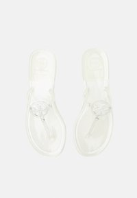 Sandales tongs transparentes avec logo décoratif rond sur les brides, semelles plates et semelles intérieures texturées, vues de dessus sur fond blanc.