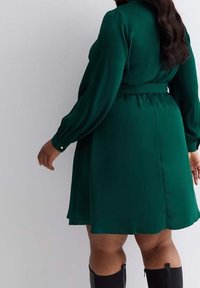 Green, long-sleeve dress in a smooth fabric with a fitted waist and flared skirt. Includes buttons on the sleeves and a tie belt.