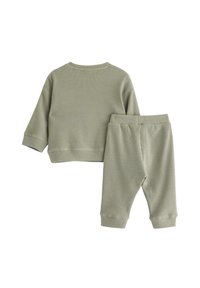 Zweiteiliger Anzug in hellem Grün, bestehend aus einem strukturierten, gerippten Stoff. Das Oberteil hat lange Ärmel und einen runden Halsauschnitt; die Hose verfügt über einen elastischen Bund.
