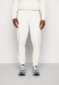 Hvid bomulds-hættetrøje og matchende sweatpants med elastisk talje, parret med grå og sorte træningssko. Glat tekstur, afslappet pasform.