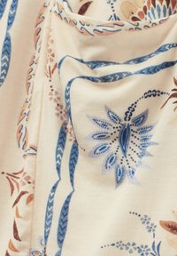 Bloemenpatroon op stof in crème met blauwe, bruine en lichtblauwe accenten. Kenmerkt zich door ingewikkelde bloemen- en bladdesigns met een gladde textuur.