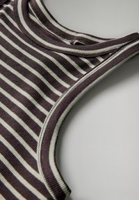 Bikses bez lences ar ribota auduma dizainu, kurā ir horizontālas svītras tumši brūnā un gaiši bēšā krāsā, ar kontrastējošu pelēku apdari ap kakla izgriezumu.