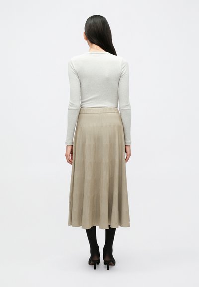 Ανοιχτό γκρι ριμπ μπλουζάκι με μακριά μανίκια σε συνδυασμό με μπεζ πλισέ φούστα μήκους μέχρι το γόνατο. Η φούστα έχει υφή και είναι ψηλόμεση.