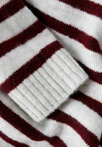 Tissu de pull tricoté à rayures rouges et blanches montré de près, avec un poignet côtelé et une texture douce et duveteuse.