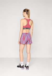 Sutiã desportivo vermelho com faixa preta da Puma, calções estampados multicoloridos, meias brancas e ténis pretos com detalhes em rosa. Textura suave.