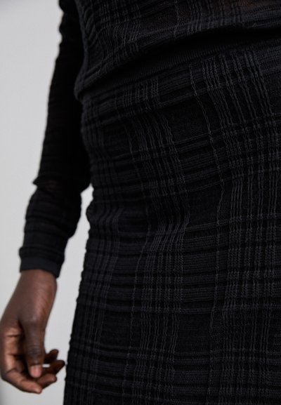 Top de punto negro texturizado con mangas largas, que presenta un diseño estampado con líneas horizontales y verticales, de silueta ajustada.