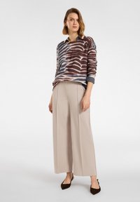 Sweter z długim rękawem w brązowe, niebieskie i kremowe paski; w połączeniu z beżowymi spodniami o szerokich nogawkach i ciemnobrązowymi płaskimi butami.