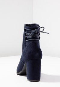 Granatowe zamszowe botki za kostkę z wysokim słupkowym obcasem. Posiadają sznurowanie z tyłu oraz gładką fakturę.