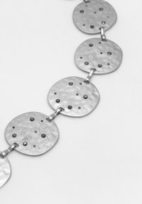 Colier din metal argintiu cu discuri circulare ciocănite și accente de puncte negre. Verigile leagă discurile, creând un aspect texturat.