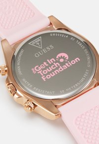 Montre en acier inoxydable rose doré avec un bracelet en silicone rose ; présente un dos argenté réfléchissant gravé de "Get In Touch Foundation."