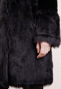 Sort faux fur frakke med en blød, langhåret overflade. Har en lige pasform og brede manchetter, som fremhæver den rike sorte nuance.