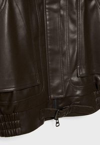 Giubbotto in pelle marrone con texture liscia, chiusura con zip e dettagli arricciati all'orlo. Presenta cuciture diagonali e tasche applicate.