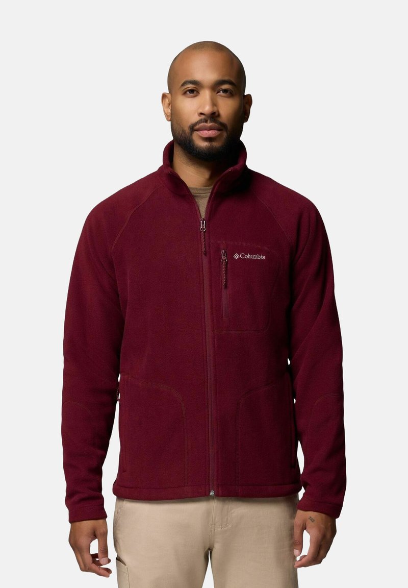 Giacca in pile bordeaux con colletto alto, chiusura con zip e due tasche laterali. Logo Columbia ricamato sul petto. Texture morbida.
