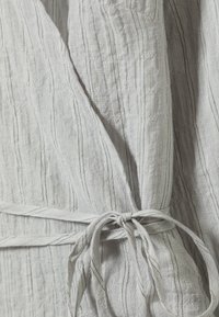 Tissu gris clair avec des rayures verticales noires, présentant une surface texturée et un accent de ceinture nouée. Matériau doux et respirant.