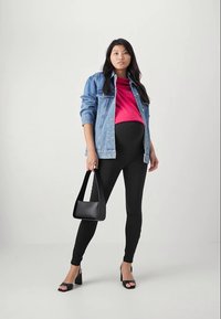Denim jacket over hot pink top, black leggings, and black handbag. High-heeled sandals. Model standing against a neutral background.