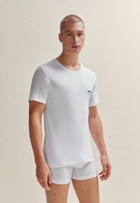 T-shirt en coton blanc à col rond et manches courtes, associé à un short boxer blanc. Présente un petit logo "BOSS" noir sur la poitrine.