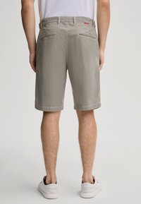 Pantaloni corti beige a fantasia con taglio dritto, tasche posteriori e un'etichetta con logo visibile; abbinati a scarpe bianche su uno sfondo neutro.