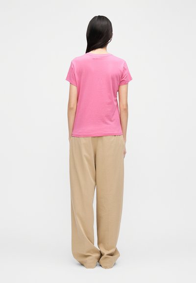 Rózsaszín pamut póló rövid ujjakkal, laza szabású és kerek nyakkivágással, lazán bézs nadrággal párosítva. Hátsó nézet, sima textúra.