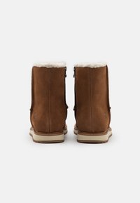 Botas de tobillo de ante marrón con forro de piel sintética blanca, cremalleras laterales y suelas de goma crema, con logo grabado en el talón.