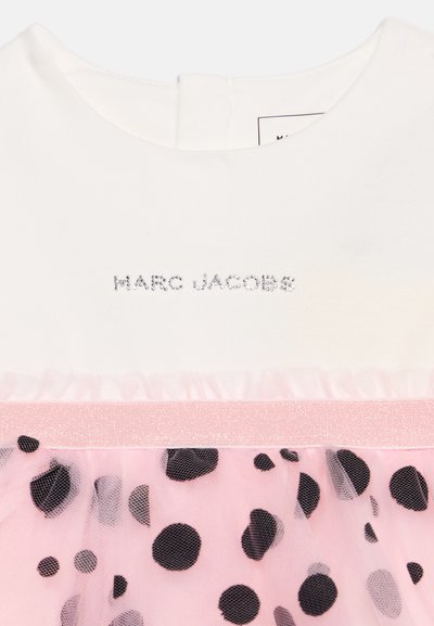 Λευκό τοπ με το "MARC JACOBS" σε μικρά κρυστάλλινα γράμματα πάνω από μια ροζ μέση και ροζ τούλινη φούστα με μαύρες βούλες.