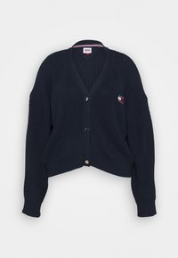 Granatowy krótki kardigan z dekoltem w kształcie litery V, zapinany na guziki, o prążkowanej fakturze. Posiada małą naszywkę z logo na lewej piersi.