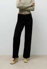 Mustad laiad teksapüksid kõrge vöökohaga, esi-taskud ja klassikaline teksakanga tekstuur. Sobitatud heleda beeži sisetallaga kontsadega.