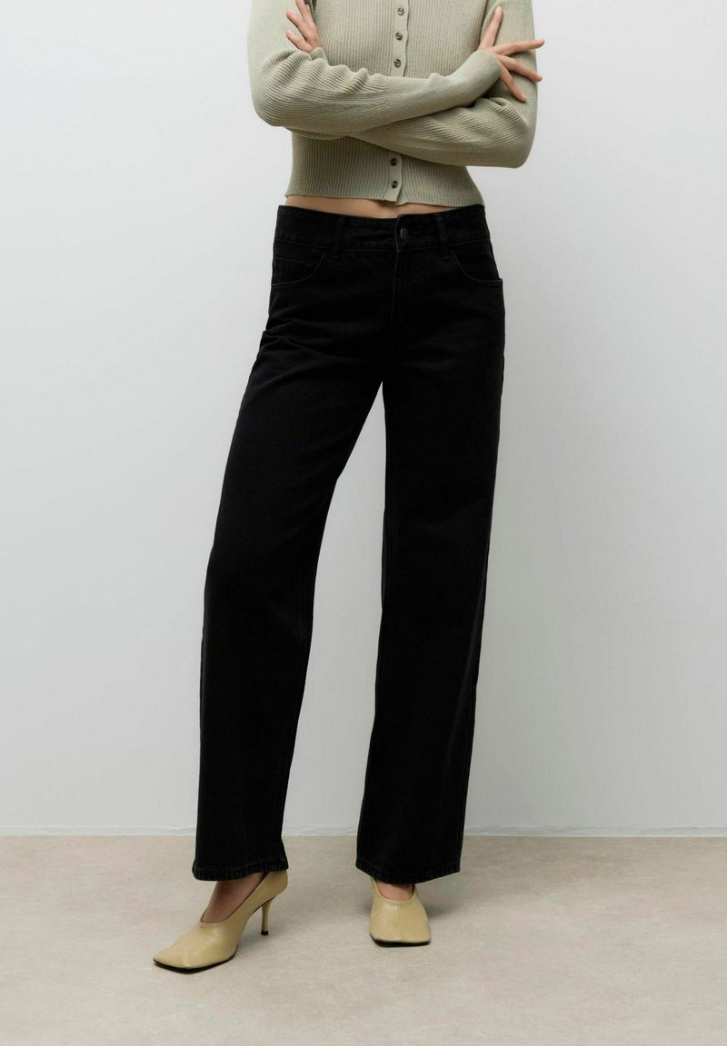 Mustad laiad teksapüksid kõrge vöökohaga, esi-taskud ja klassikaline teksakanga tekstuur. Sobitatud heleda beeži sisetallaga kontsadega.