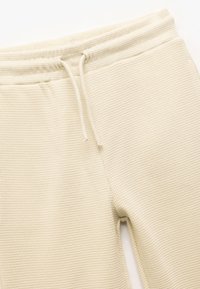 Beżowe joggery z dzianiny waffle z elastycznym paskiem i sznurkiem do regulacji. Charakteryzują się teksturowanym materiałem, który zapewnia miękki i przewiewny design.